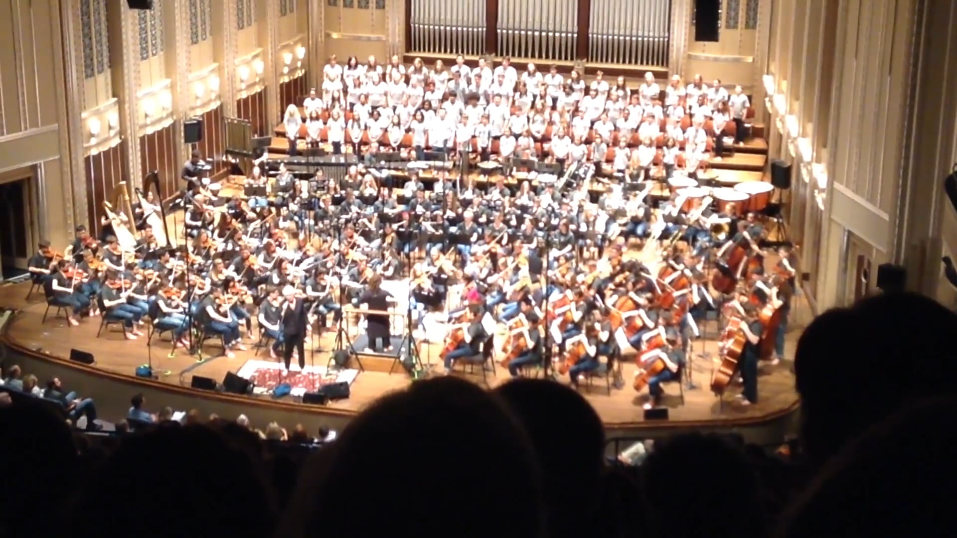 Full orchestra and choir performing on stage in a grand concert hall, part of a Cleveland Youth Orchestra event