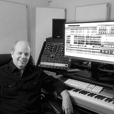 Linwood Bell, composer and arranger, seated in his Las Vegas studio in front of a digital audio workstation and mixing equipment in a black and white photo.