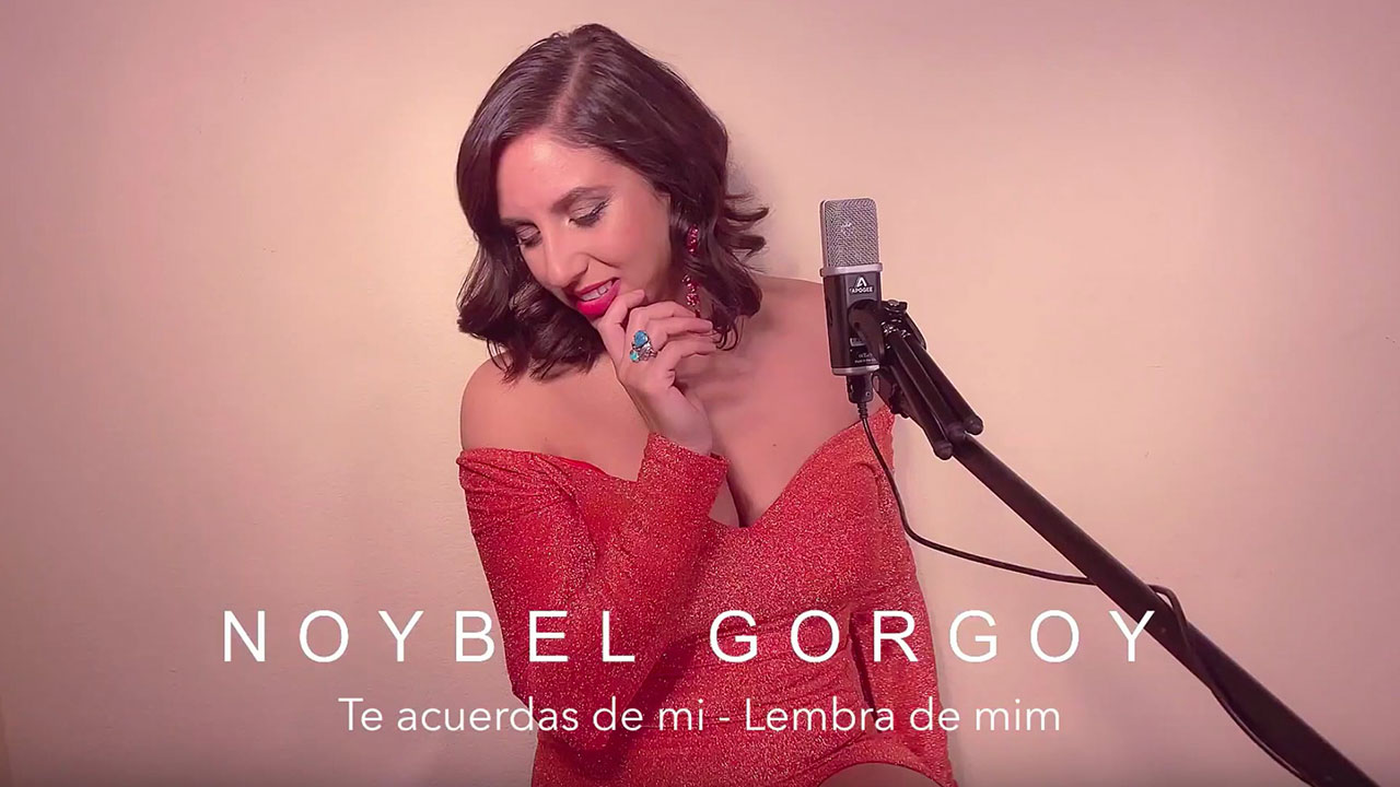 Noybel Gorgoy performs in a sparkling red dress, standing at a microphone with closed eyes and a graceful smile