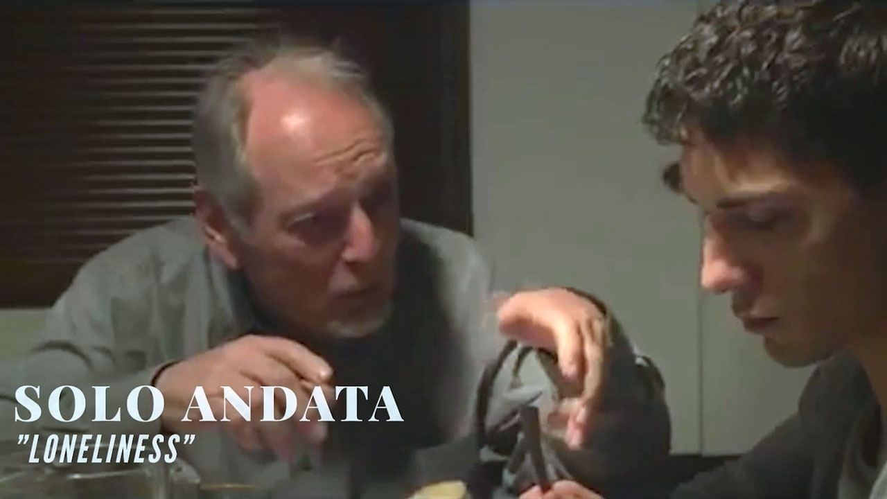 Elderly man and young man sitting at a table having an intense conversation, scene from the short film Solo Andata titled “Loneliness.”